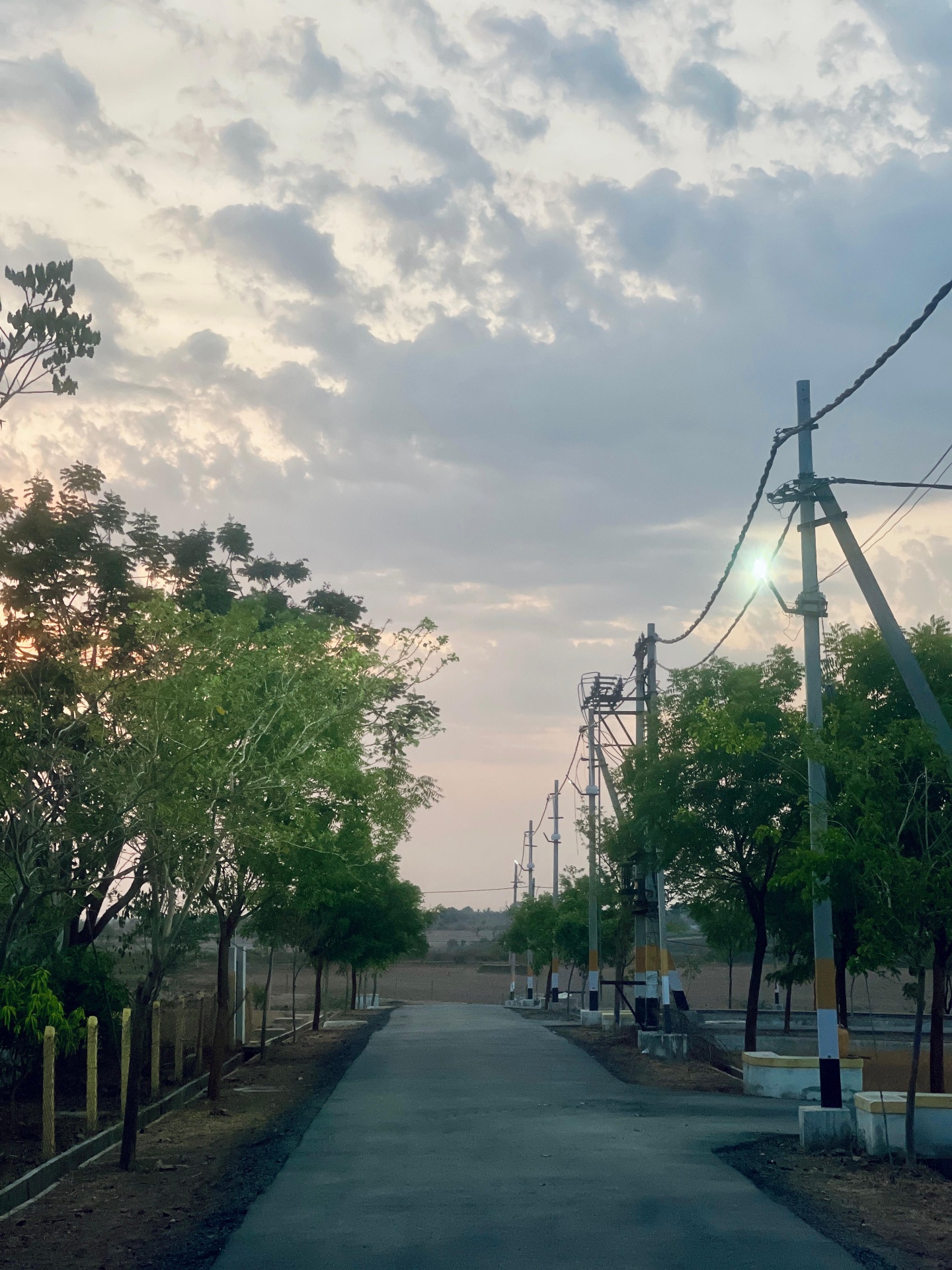 Evening view of an internal road with HESCOM electrification poles and painted kerbs at Sri Krishna Valley